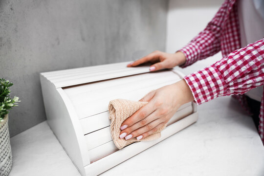 Woman wiping dust from breadbox at white marble countertop in kitchen, closeup