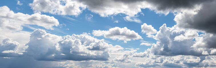 Obraz premium Panoramic view of a bright blue sky with voluminous white and grey cumulus clouds on a sunny day creating a sense of space and freedom