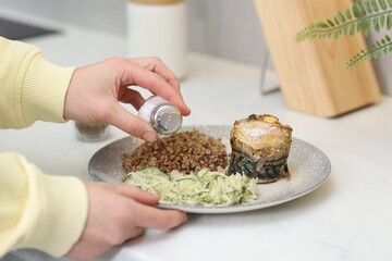 Woman salting buckwheat with salad and mackerel roll at white table indoors, closeup