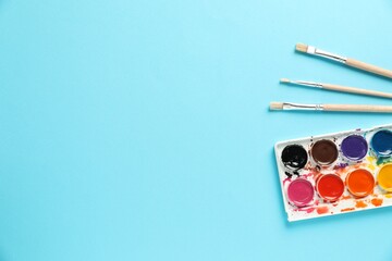 Watercolor palette and brushes on light blue background, flat lay. Space for text