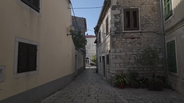Walking along an romantic alley between charming historic apartments made of time-worn stones in the old town of Porec, Croatia. Mediterranean house exterior on sunny summer afternoon.