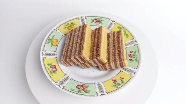 Slices of traditional Indonesian lapis legit layer cake rotating on a plate. Delicious sweet dessert isolated on white background.
