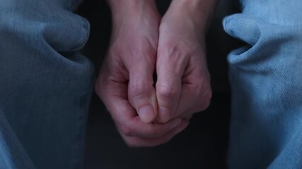 A middle-aged man clasping his hands together in his lap, conveying emotions of anxiety, stress, or contemplation. Close up.