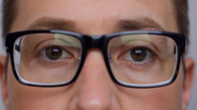 Close view of adult eyes wearing black eyeglasses with neutral expression and sharp lens reflections