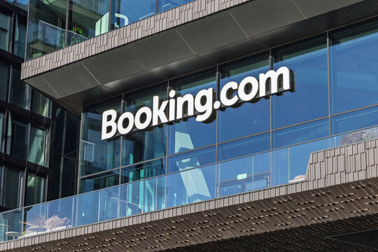 Close-up view of the large white Booking.com logo attached to the glass facade of their modern headquarters office building. Amsterdam Netherlands, 28 december 2025