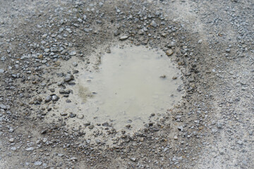 small puddle of muddy water in gray gravel and stones on construction site ground with wet soil and rocks after rain outdoor industrial environment infrastructure.