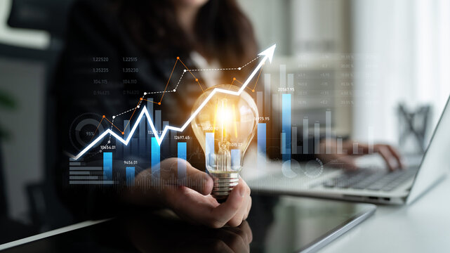 A businesswoman holds a light bulb symbolizing innovation while surrounded by charts and graphs depicting growth and financial metrics in a modern office setting. Scalp - Powered by Adobe