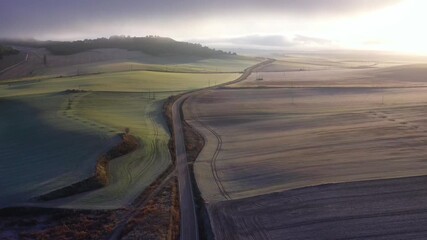 Drone Flying Slowly Forward Over Rural Road and Winter Farmland at Sunrise With Distant Fog