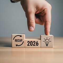 Flipping a cube to reveal '2026' next to a lightbulb icon, signifying a future vision and a recap of past events, all presented in a studio setting with a blurred background