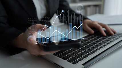 A businessman analyzes financial data on his laptop while using a smartphone. Virtual graphs and charts illustrate trends in a modern office setup, showcasing technology role in business. Scalp