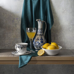 Still life with lemons, a wine glass, an elegant jug, and a cup of tea in yellow, white, blue, and green tones