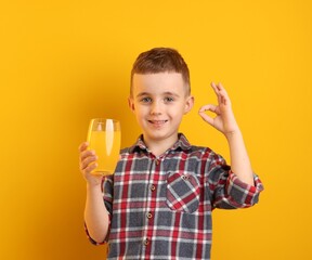 Happy boy with glass of juice showing okay gesture against yellow background