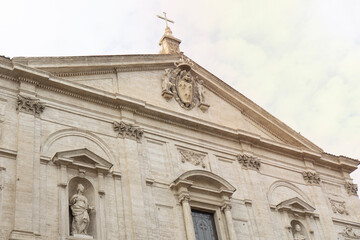 Fototapeta premium Low angle view of historic Catholic church facade in Rome, Italy, with stone statues and cross, reflecting classical European religious architecture.