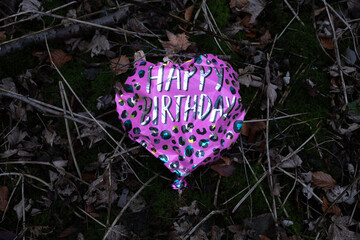 Deflated foil heart-shaped balloon with 'Happy Birthday' on forest floor.