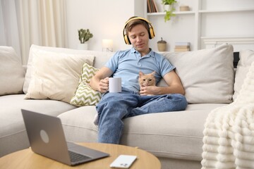 Obraz premium Man in headphones with his cute cat and mug on sofa at home