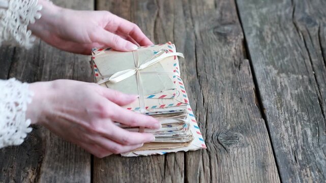The woman places a stack of paper letters tied with a decorative ribbon on a wooden table.