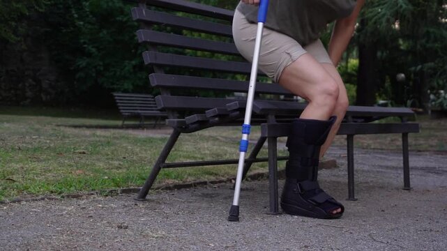 An unrecognizable woman uses orthopedic medical fracture Walker to walk and exercise in the garden after a fractured leg, undergoing rehabilitation. Orthopedic support splint foot stabilize