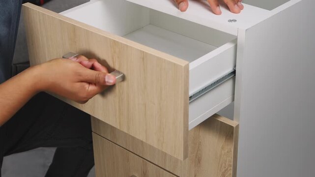 Professional carpenter opening and closing a wooden drawer to verify smooth movement and proper function, representing quality control, craftsmanship, furniture making, woodworking skills, and attenti
