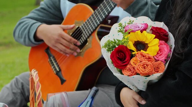 Romantic scene at a camping picnic where a man plays a song on his guitar while his girlfriend listens attentively and holds a bouquet of flowers, expressing love and emotional connection in nature.
