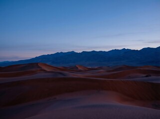 Fototapeta premium Red desert dunes meeting a dark blue mountain range at twilight