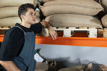 Tired make warehouse worker is leaning shelf. Young man in a warehouse.
