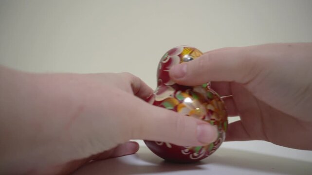Hands open the matryoshka doll. Wooden folk toy, painting, close-up on a light background, subject shooting. A matryoshka doll made of 9 nesting dolls.