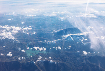 Majestic aerial view shows snow-capped mountains above an Alpine lake, Sierra Nevada range. Sunlight filters through clouds, highlighting the rugged landscape view from above