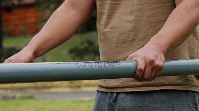 Man stretching his body on parallel bars, moving forward and backward during an outdoor workout, showing flexibility, recovery and body control in a public park.