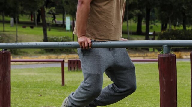 Man performing pull ups on parallel bars at an outdoor gym, showing strength, effort and physical training in a public park environment.