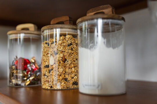 Glass storage jars with granola and sweets on wooden shelf