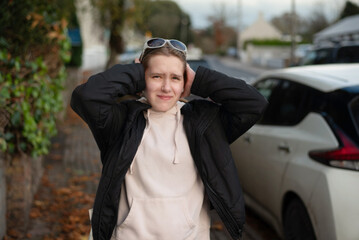 A young pretty girl is tired of city noise, traffic and her head starts to hurt, she covers her ears at urban street