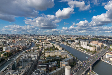 Fototapeta premium A panoramic view captures the vibrant city of Moscow, with bustling streets, the winding river, numerous buildings, and a bright blue sky filled with clouds.