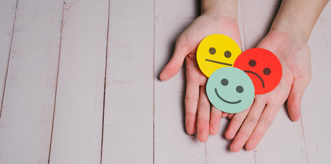 Feedback concept. Happy face Sad face Neutral face Emotion Paper cutouts Hand holding Wooden background Positive emotion Negative emotion Mixed feelings