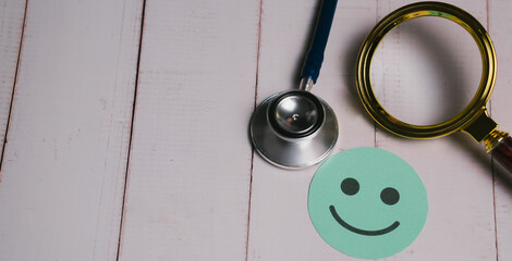 Feedback concept. Stethoscope and magnifying glass near green paper smiley face on white wooden...