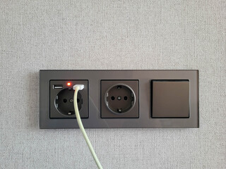 White wire and two sockets and a switch that provide access to electricity on the wall. Electrical sockets for convenient power supply in the office and at home