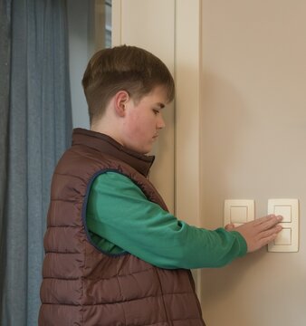Boy in a vest turning off wall switches in a living room with natural light around noon