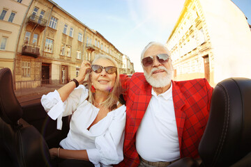 Stylish elderly couple enjoying ride in convertible car, wide angle lens