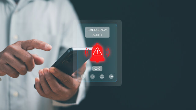 Emergency alert concept. Hand using smartphone with warning notification and alert icon on screen. Crisis notification, emergency response, risk management, mobile technology, public safety system. - Powered by Adobe