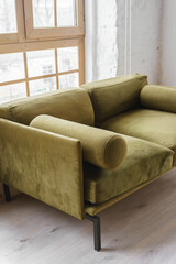 Soft khaki green velvet sofa placed near large window in bright loft interior, showing contemporary furniture design, comfort and elegant home decor style.