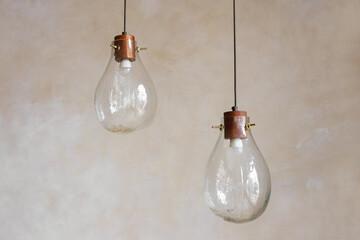 Two decorative glass pendant lamps with wooden and metal details hanging against painted neutral wall background, representing modern lighting, illumination, interior decor and handmade design.