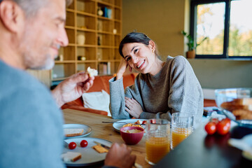 Man and woman sharing a joyful morning breakfast on a wooden table, smiling and interacting in a cozy home environment