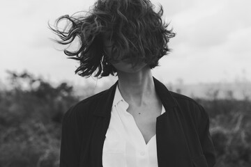 Hair blowing in the wind over an outdoor scene, a white shirt with dark jacket creates a fashion driven image with motion and mood in black and white.