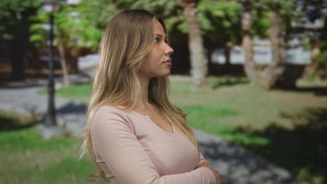Woman with blonde hair standing with crossed arms in a green park; denial rejection detachment skepticism.