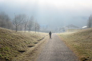 Woman walking along a gravel path in a mountain town on a foggy winter morning