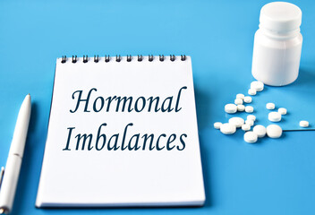 HORMONAL IMBALANCES - words in white notebook on blue background with pills and pen