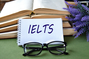 Notebook with IELTS text on a green background with books and glasses