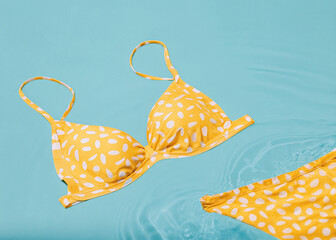 Women's swimsuit with a lively pattern floats on the surface of the water in the pool, summer vacation minimalist concept.