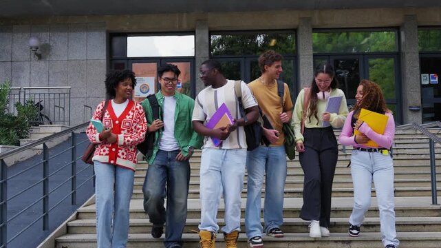 Diverse group of students walk down campus steps after class, chatting and smiling with books and backpacks. Casual university scene showing friendship, teamwork and youthful energy.