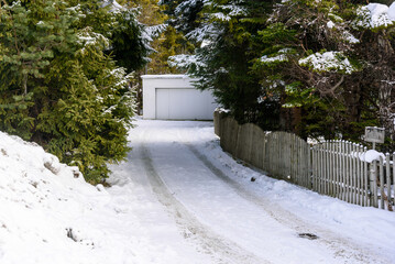 Snow covered driveway lined with a worn wooden fence to a garage on a sunny winter day