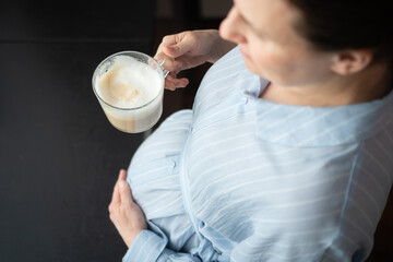 Expecting mother carefully sipping coffee at home. Balanced approach to caffeine consumption during pregnancy with doctor's approval.